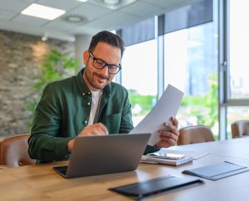 smiling man holding paper and working on laptop